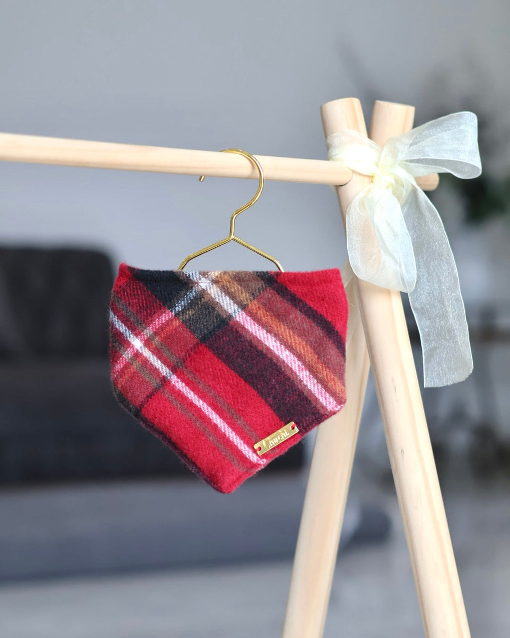 Red plaid fabric on a hanger attached to a wooden stand with a white bow against a blurred background