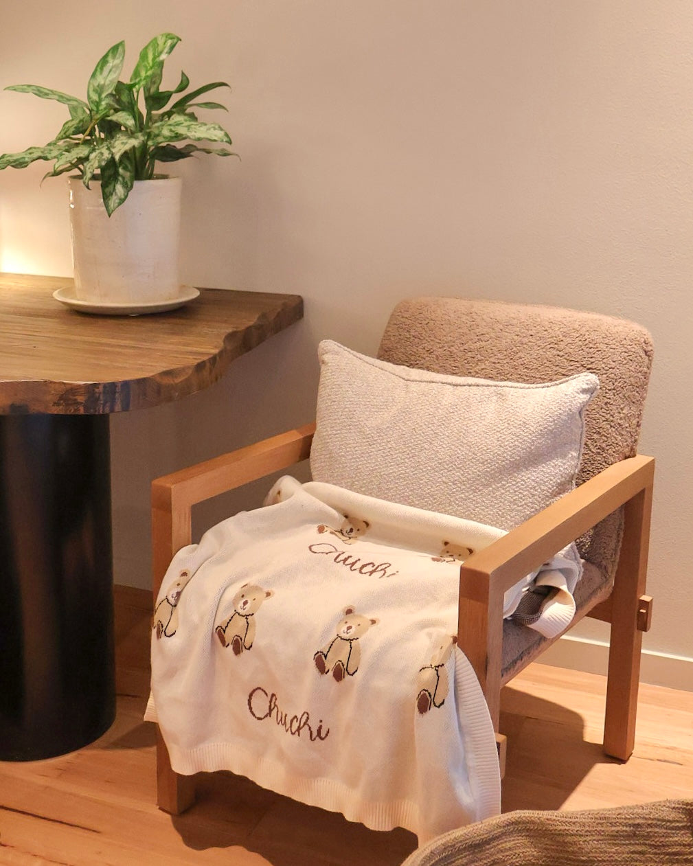 Chair with a Chuchi blanket and pillow, next to a wooden table with a plant, in a room setting.