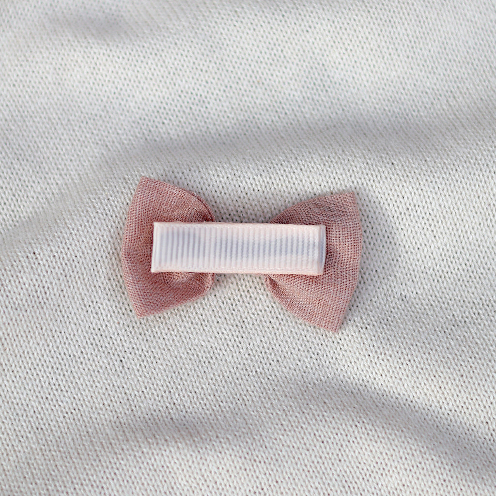 Pink bow hair clip on a white fabric background