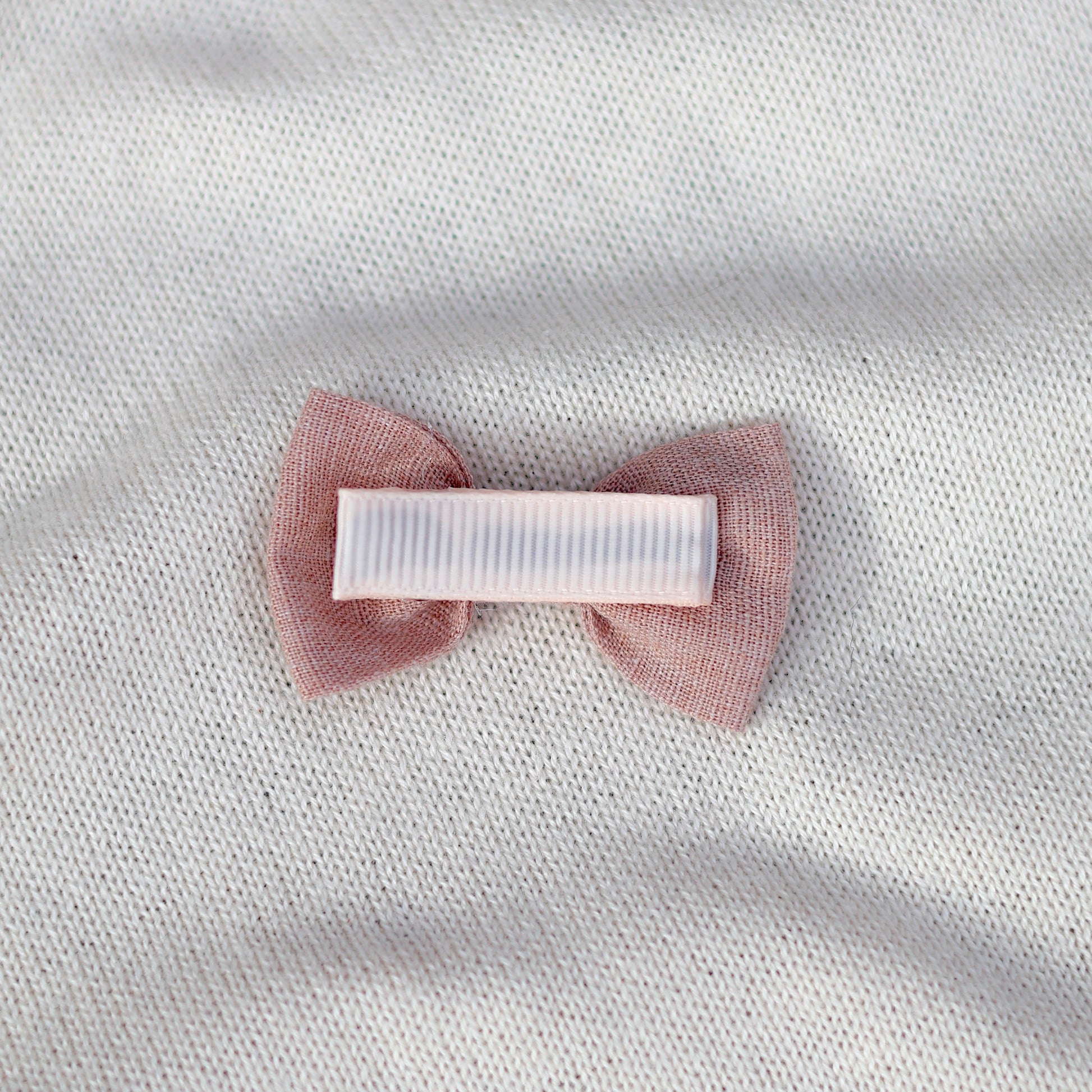 Pink bow hair clip on a white fabric background