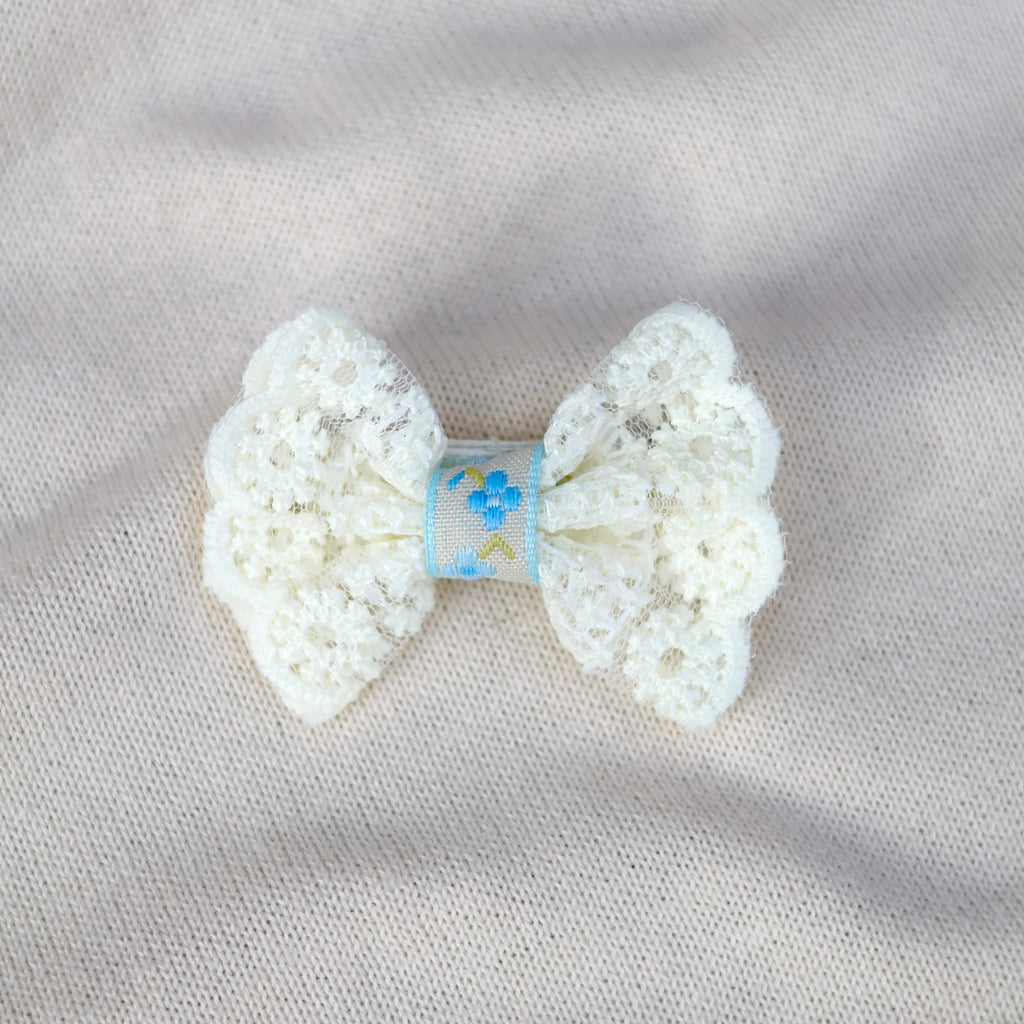 White crochet bow with a blue label on a light gray fabric background
