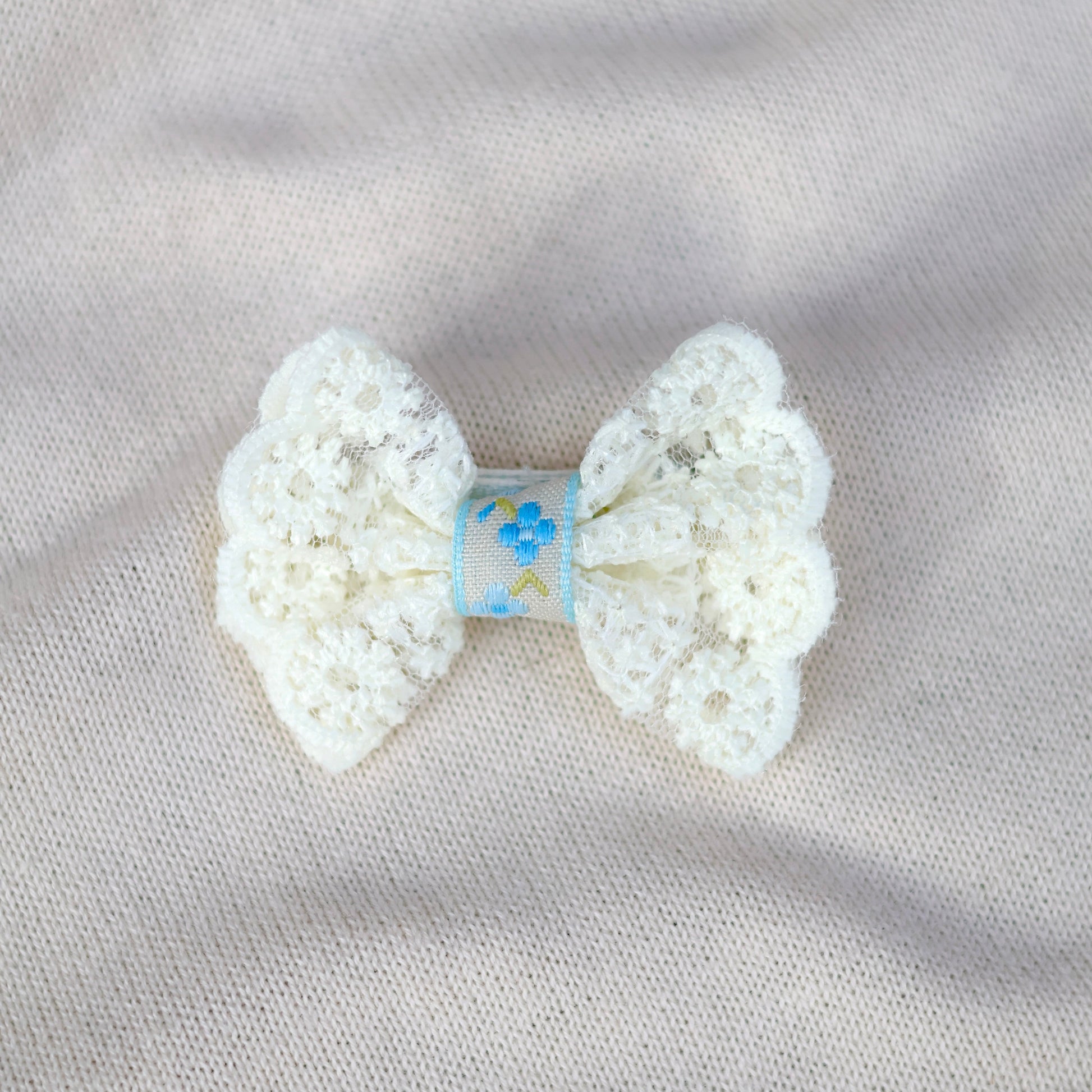White crochet bow with a blue label on a light gray fabric background