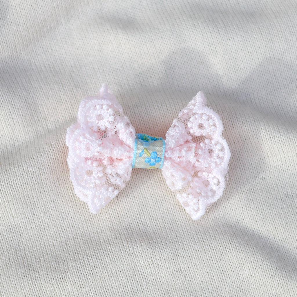 Pink lace bow hair clip on a light gray fabric background