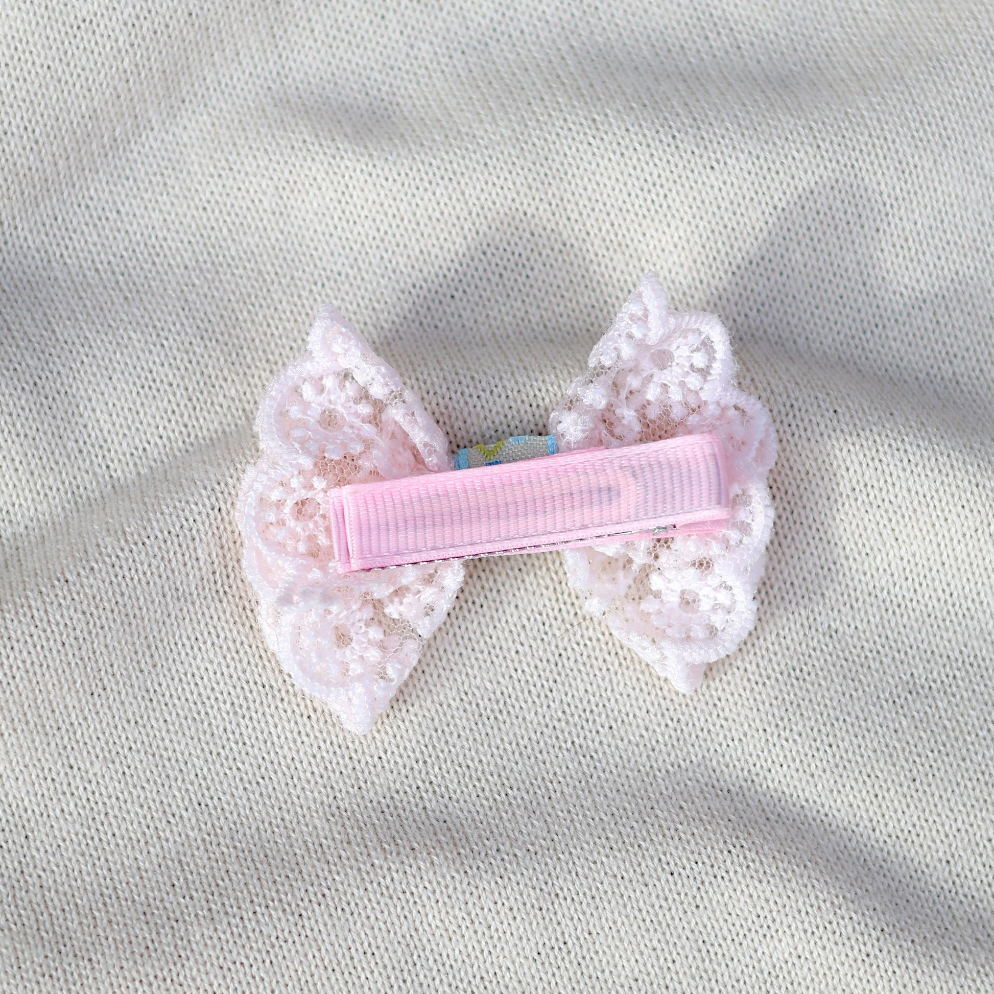 Pink hair clip with lace details on a gray fabric background