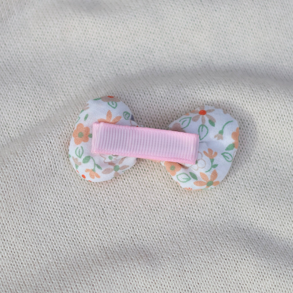 Floral-patterned hair clip with a pink center on a gray fabric background
