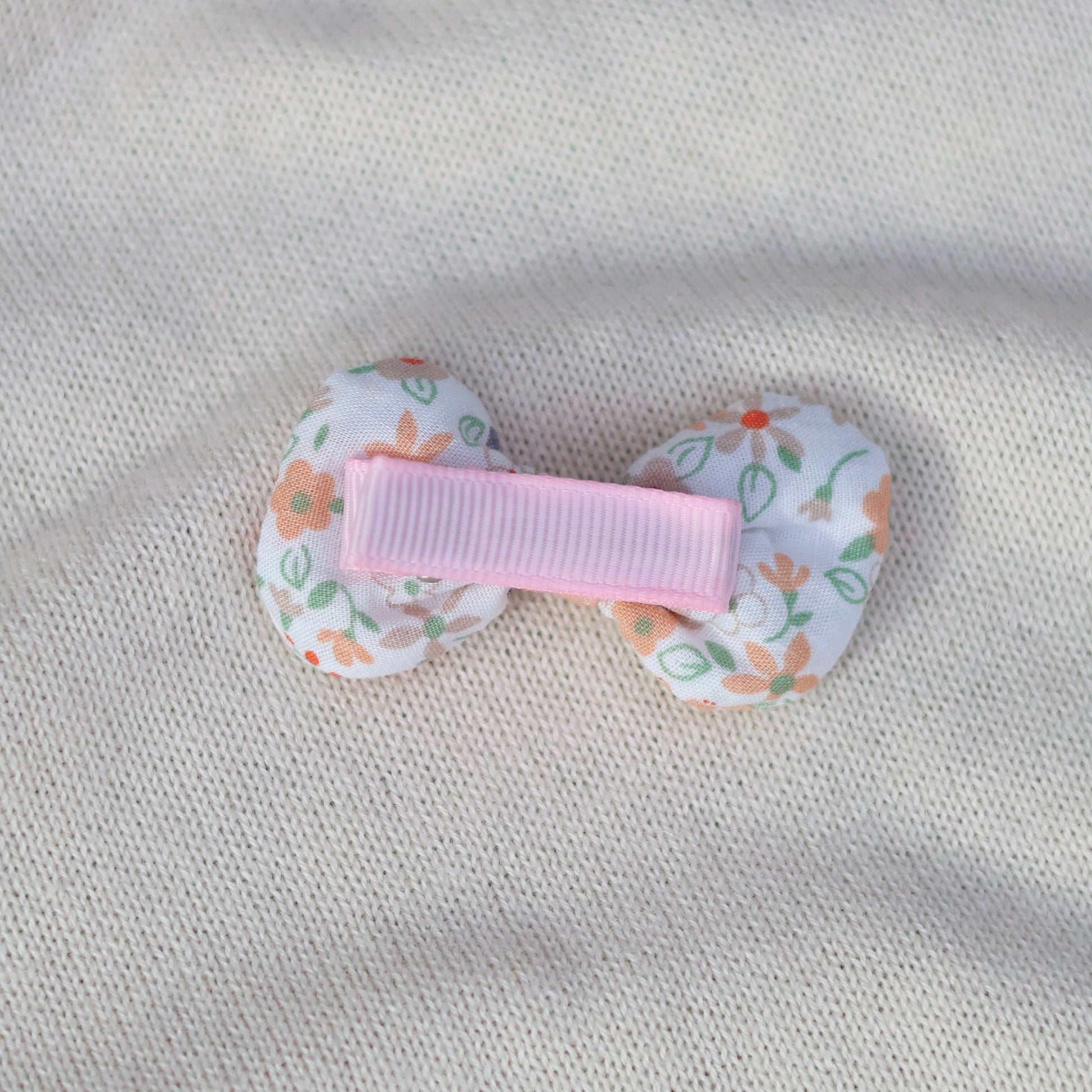 Floral-patterned hair clip with a pink center on a gray fabric background