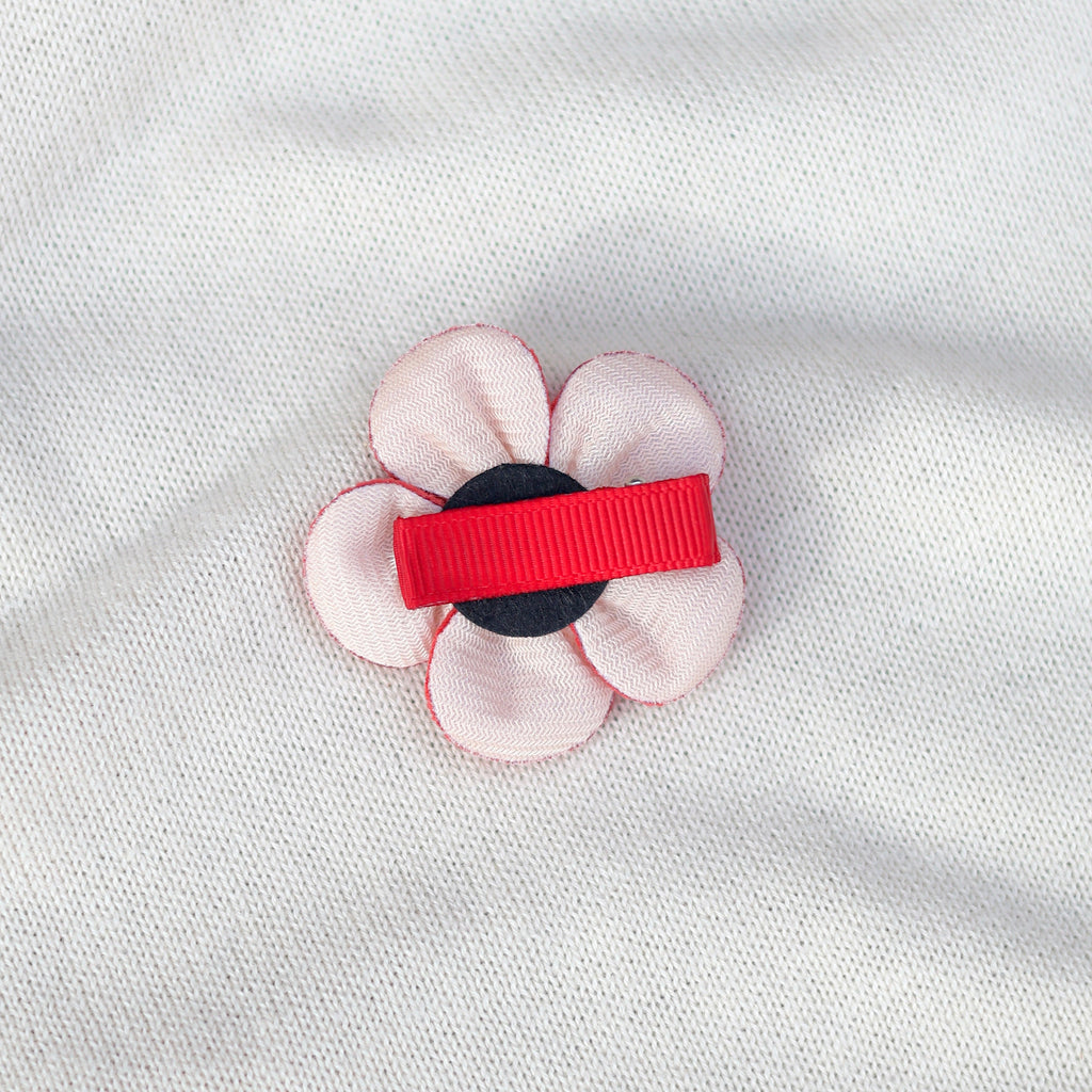 Floral hair clip with red and black accents on a white fabric background