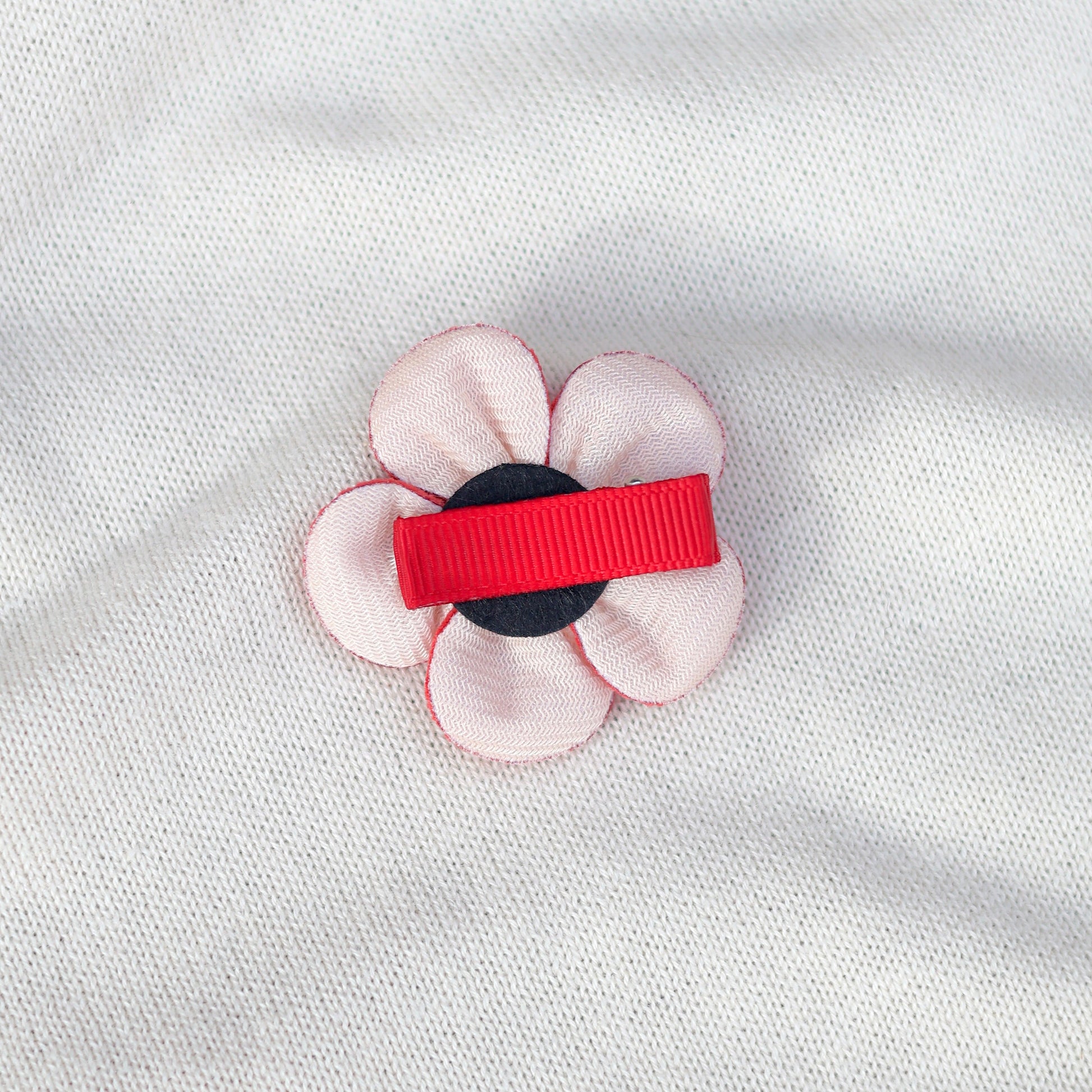 Floral hair clip with red and black accents on a white fabric background