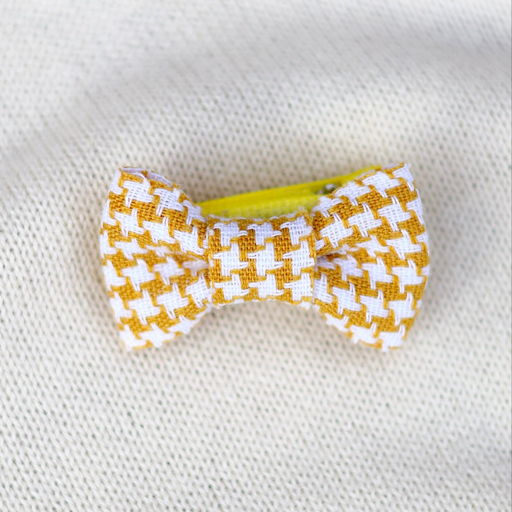 Yellow and white checkered bow hair clip on a white fabric background