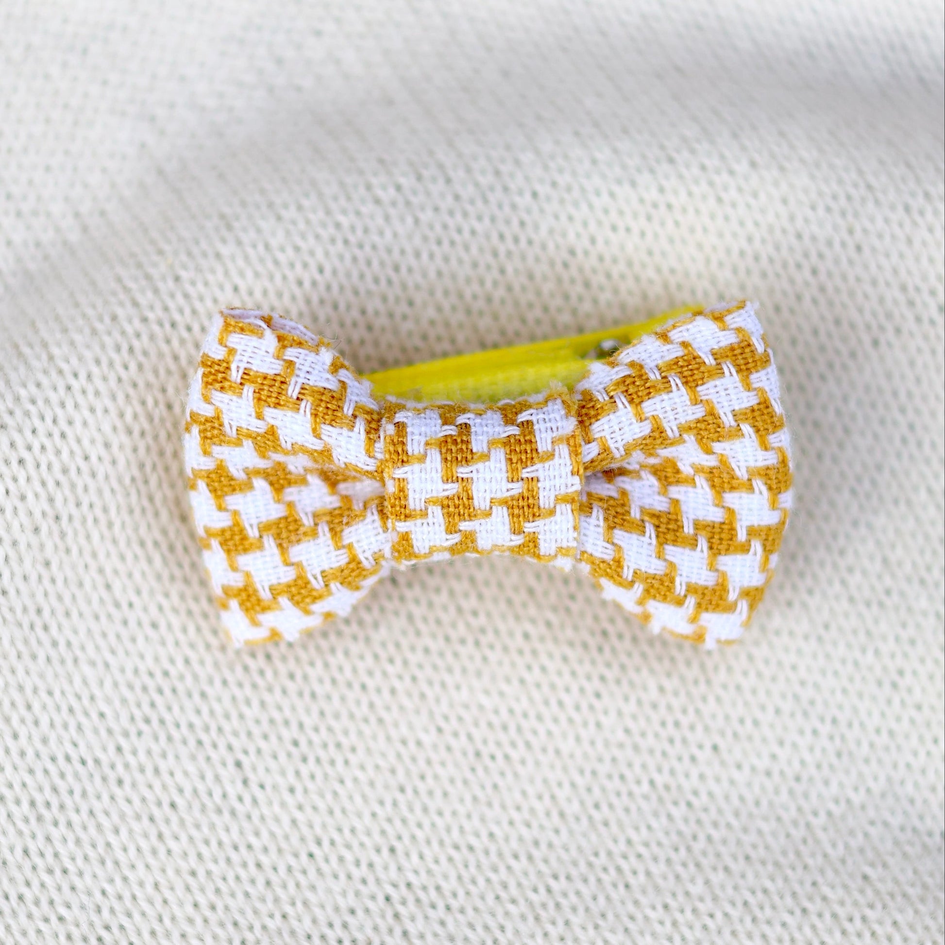 Yellow and white checkered bow hair clip on a white fabric background