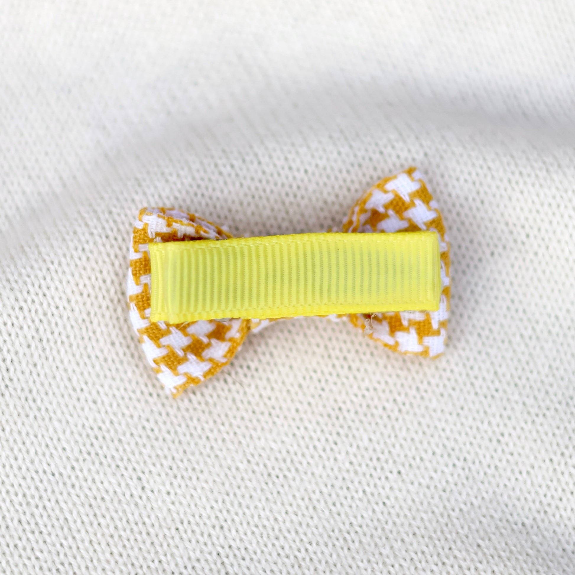 Yellow hair bow with white checkered pattern on a white fabric background