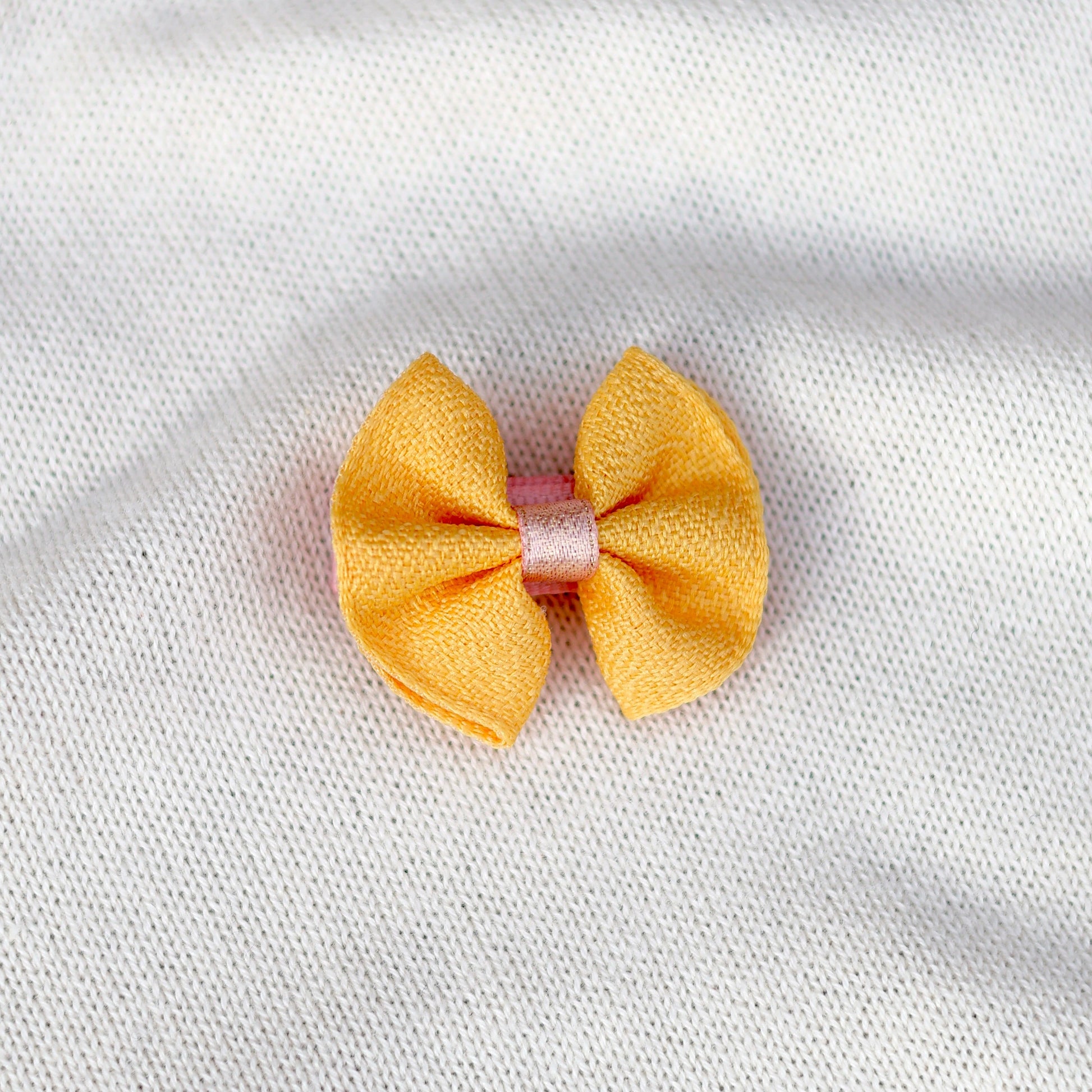 Yellow bow hair clip on a white fabric background