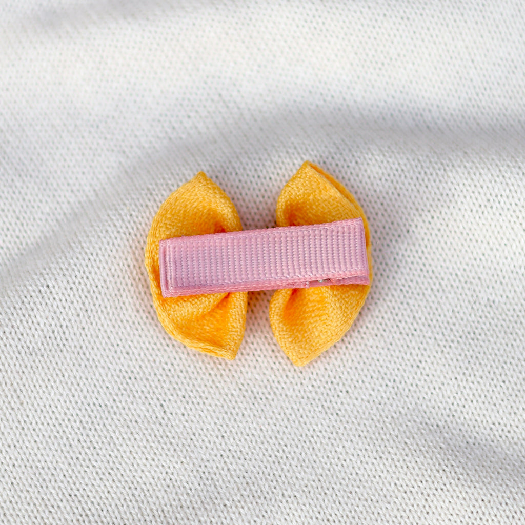 Yellow hair bow with a pink clip on a white fabric background