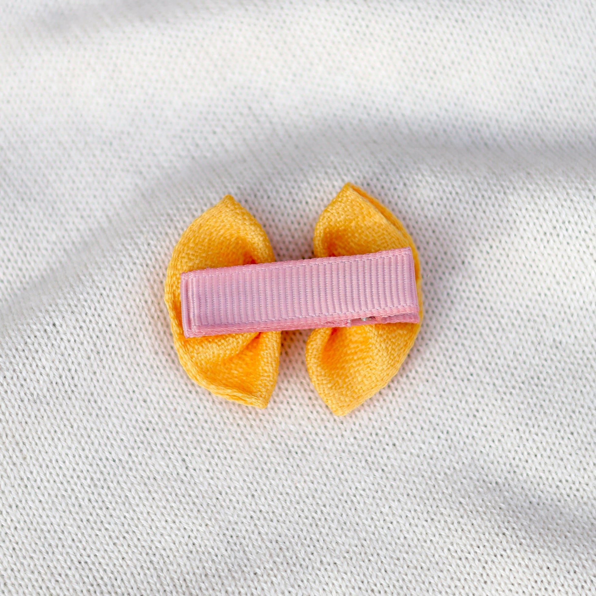 Yellow hair bow with a pink clip on a white fabric background