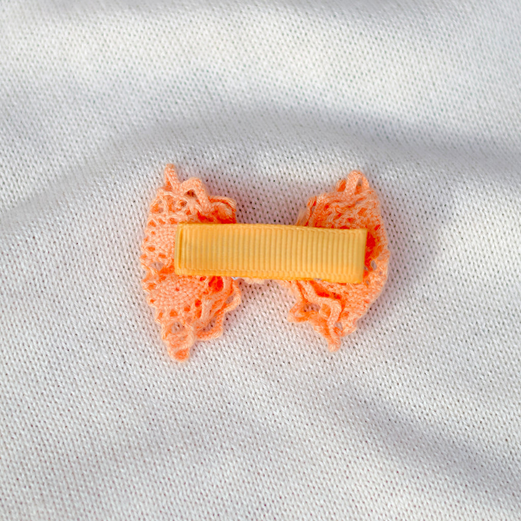Orange bow hair clip on a white fabric background