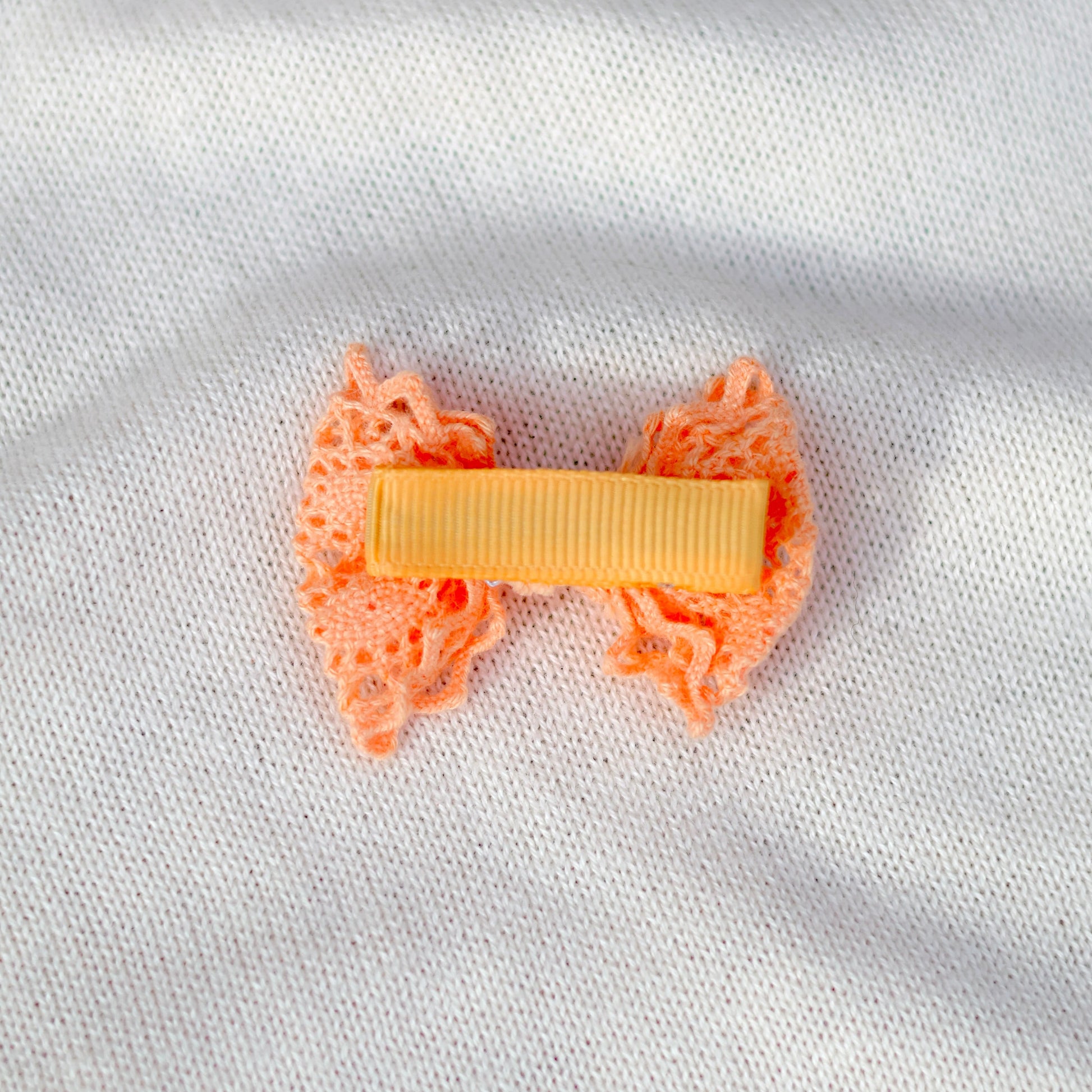 Orange bow hair clip on a white fabric background