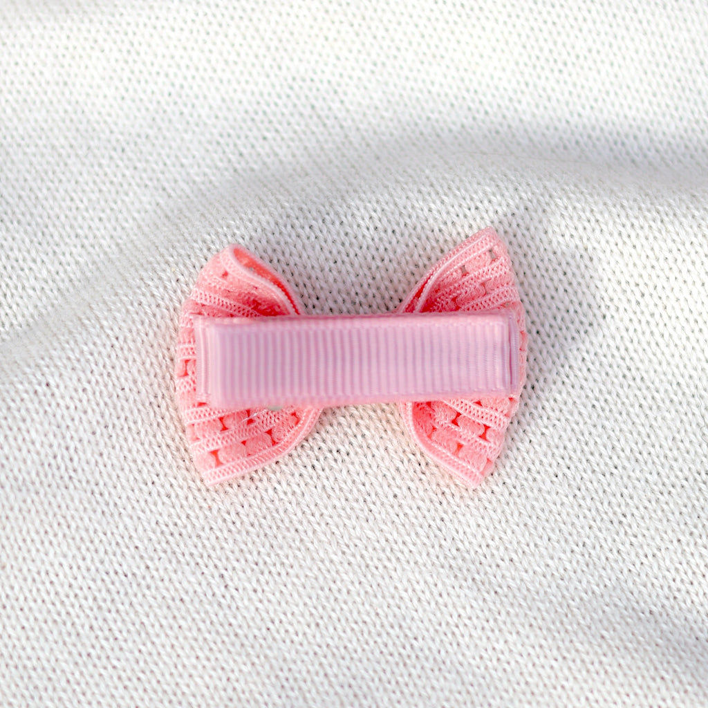 Pink bow hair clip on a white textured fabric background