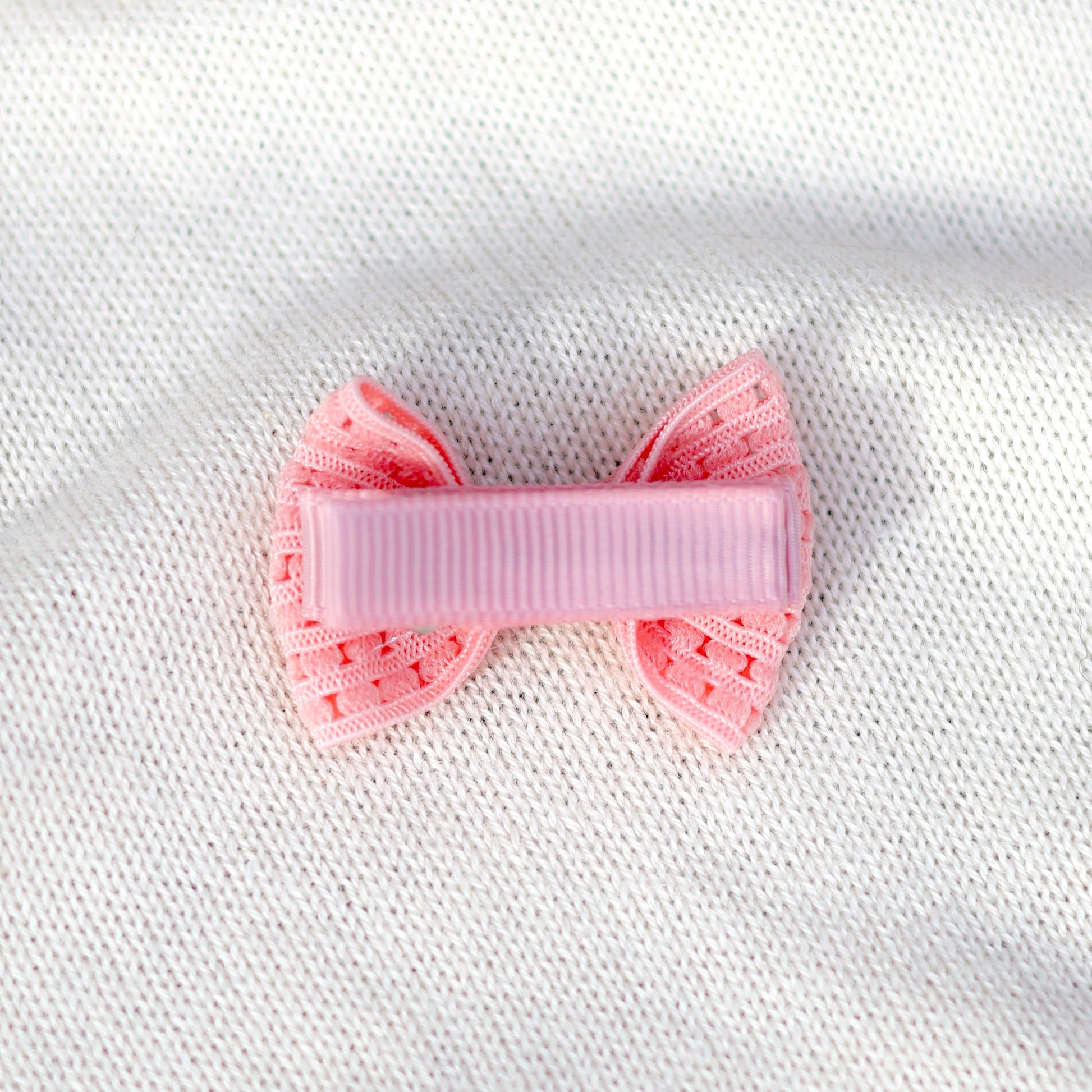 Pink bow hair clip on a white textured fabric background