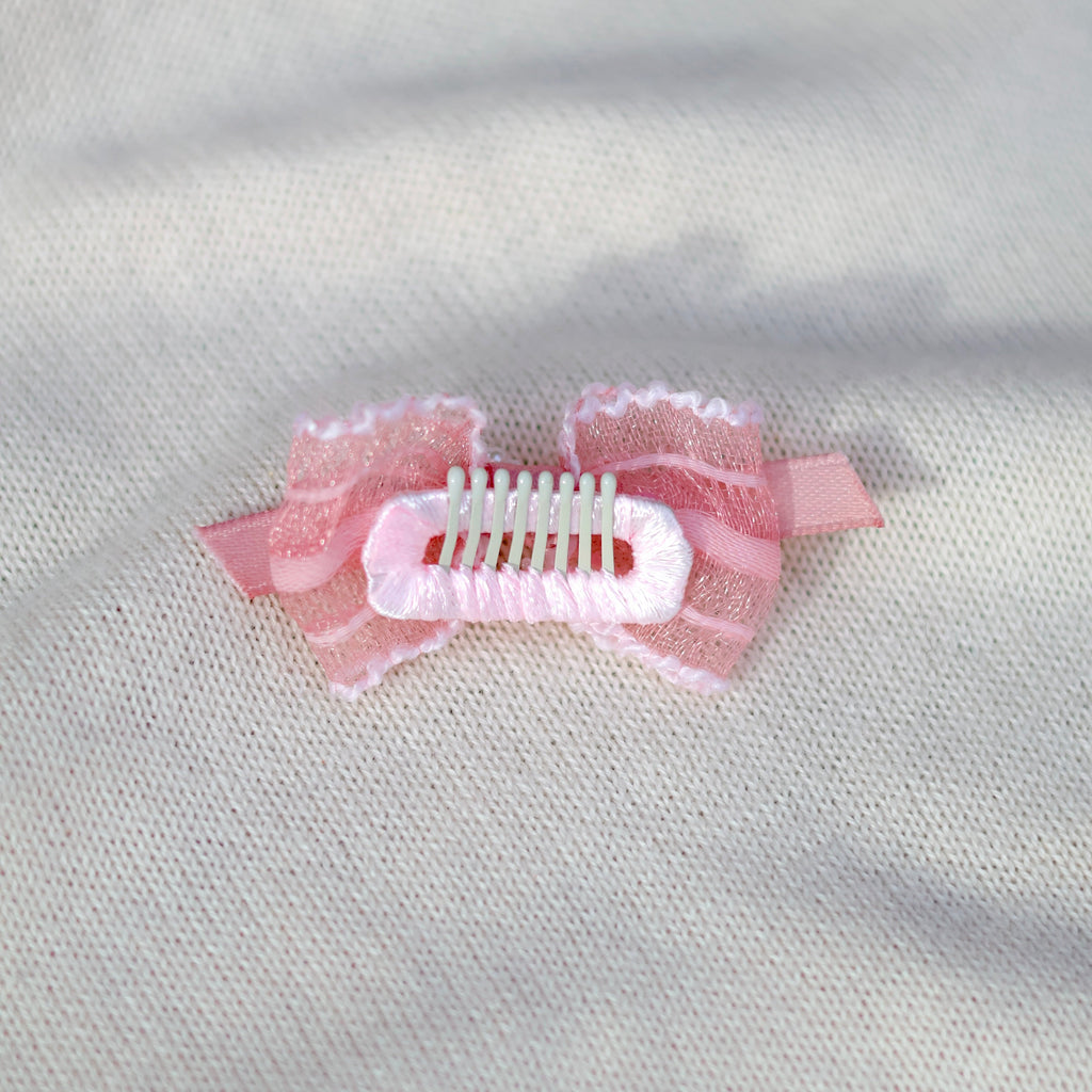 Pink hair clip with decorative elements on a light gray fabric background