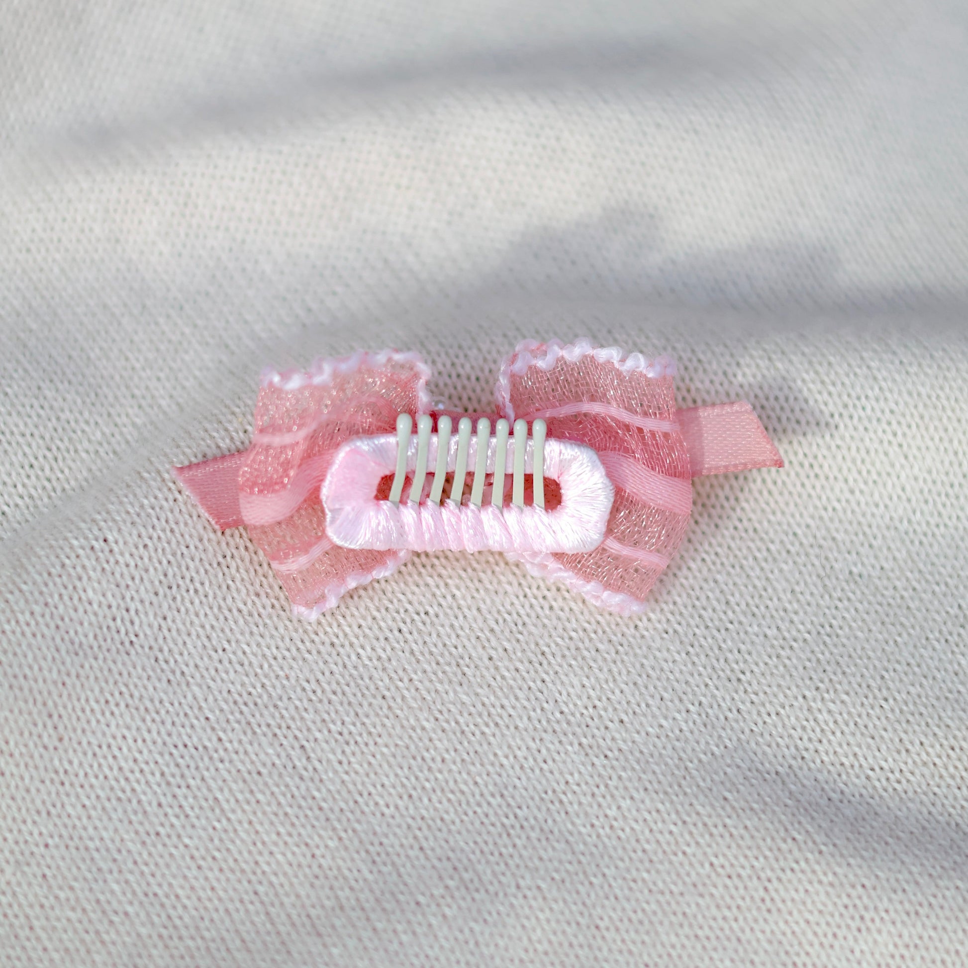 Pink hair clip with decorative elements on a light gray fabric background