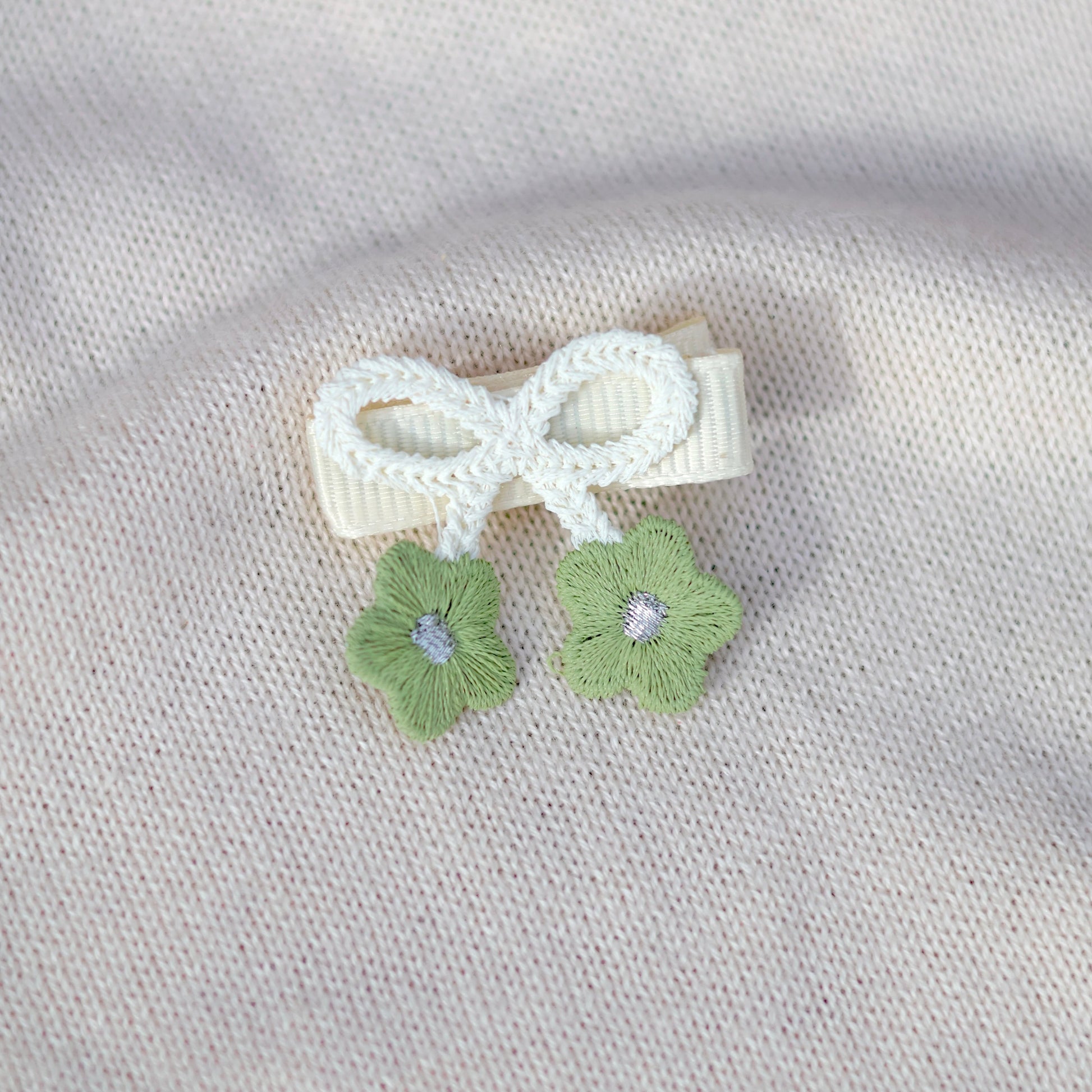 White bow hair clip with green flowers on a light gray fabric background