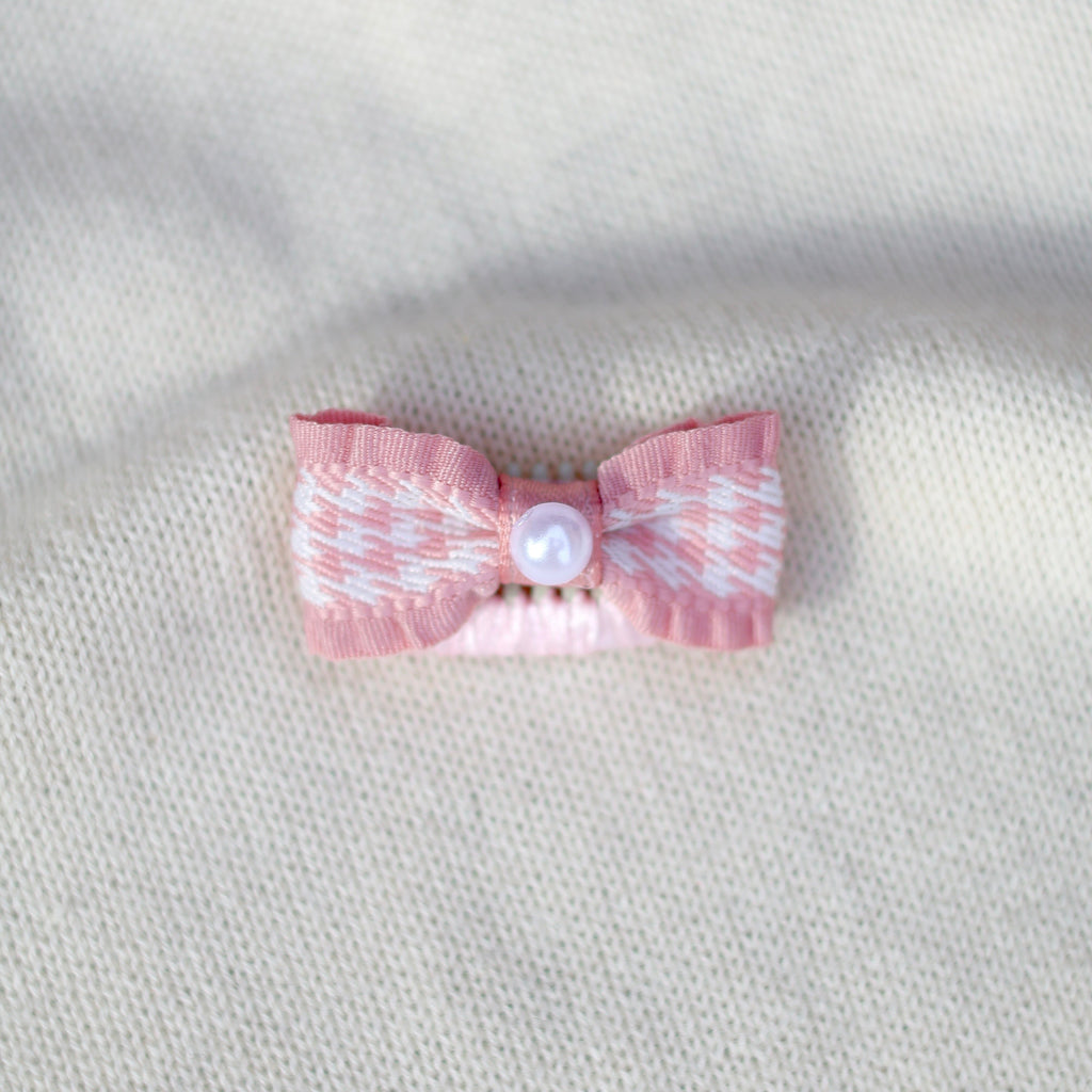 Pink bow with a pearl center on a textured gray background