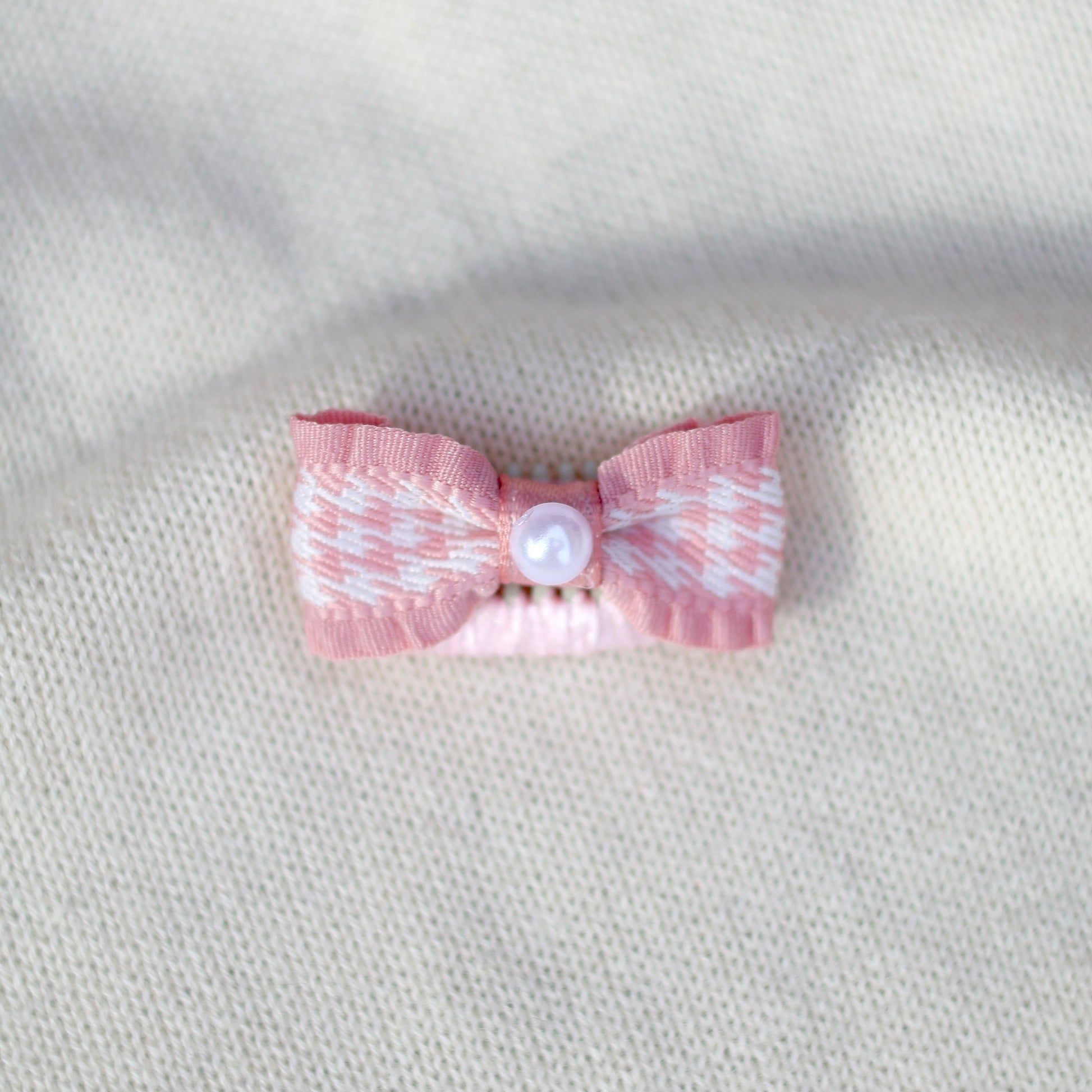 Pink bow with a pearl center on a textured gray background