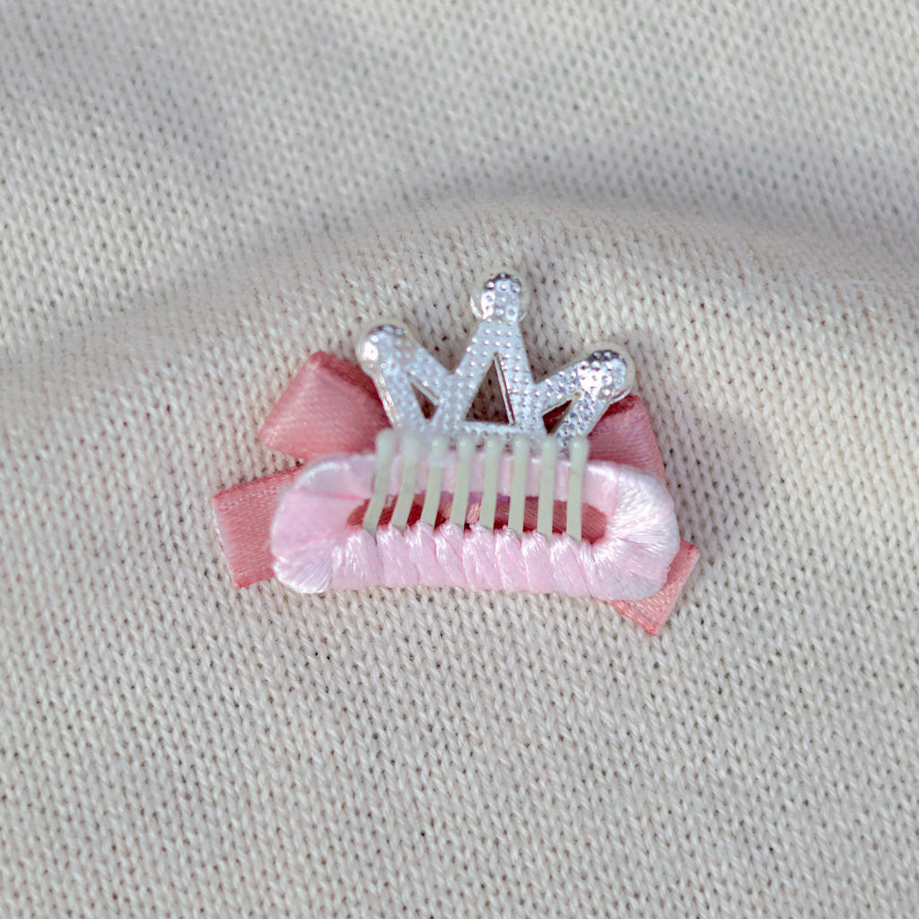 Pink hair clip with a silver tiara on a beige fabric background