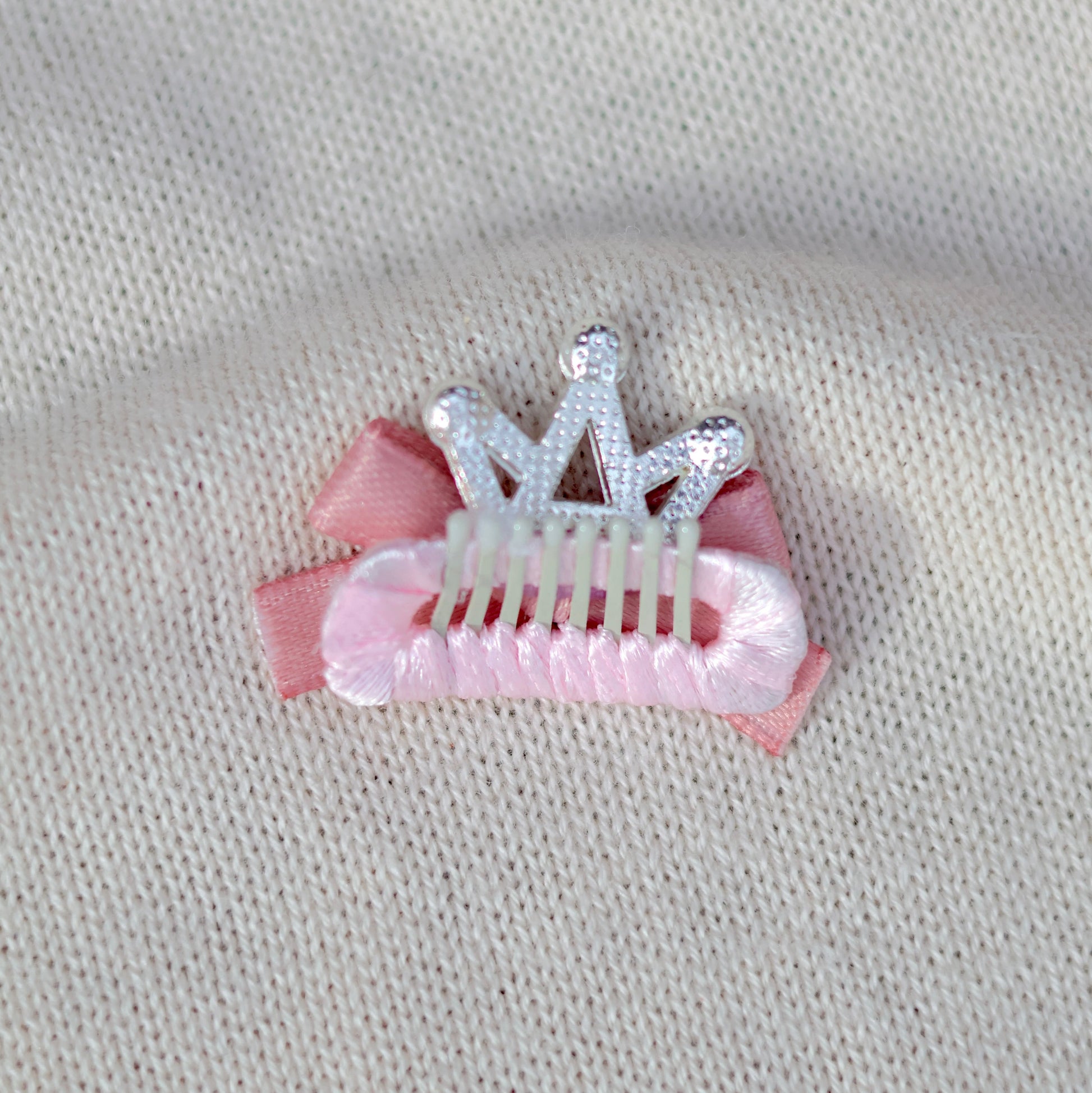 Pink hair clip with a silver tiara on a beige fabric background