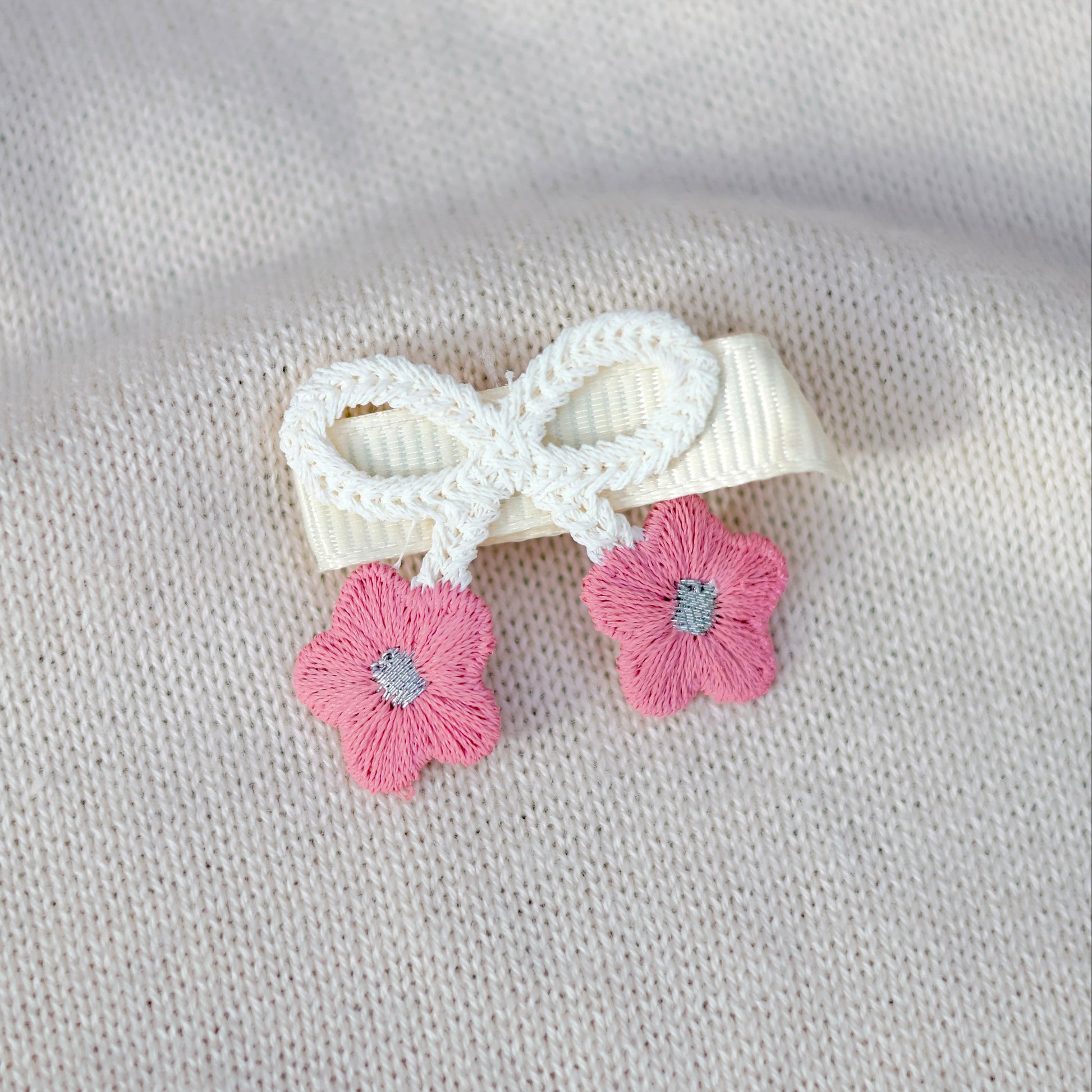 White bow hair clip with pink flowers on a beige fabric background