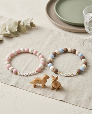 Two beaded bracelets with 'CHUCHI' on a tablecloth with dog figurines.